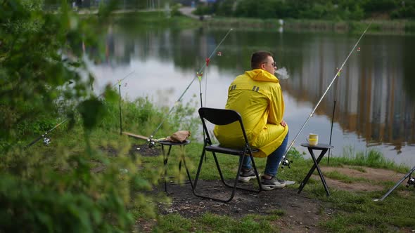 Wide Shot Young Fisherman Smoking Sitting on River Bank Waiting for Catch