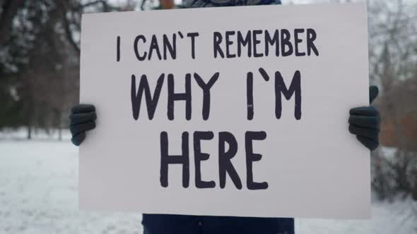 Person holds a white sign with I can't remember why i'm here statement.