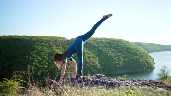 Woman in Overalls Practicing Yoga  Ardha Chandrasana on High Cliff Above Water