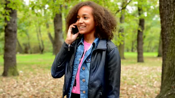 Young African Chatty Smile Girl Talks with Friend Through the Smartphone in the Forest