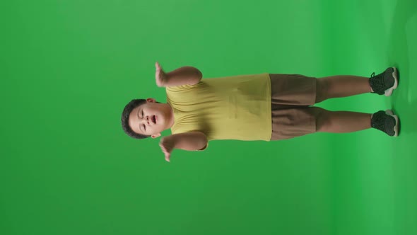 Full Body Of Smiling Asian Little Boy Blowing Kisses To A Camera In The Green Screen Studio
