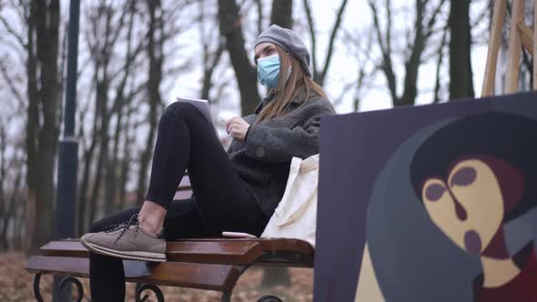 Focused Woman in Covid19 Face Mask Drawing with Pencil Admiring Sketch Sitting on Bench with Blurred