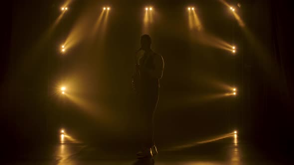 Silhouette a Young Stylish Guy Plays the Golden Shiny Saxophone in the Yellow Spotlights on Stage