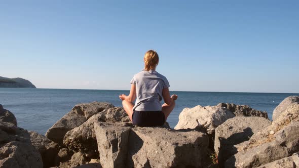 Young Woman Sits in a Lotus Position on the Seashore and Looks at the Sea Dawn of the Sun