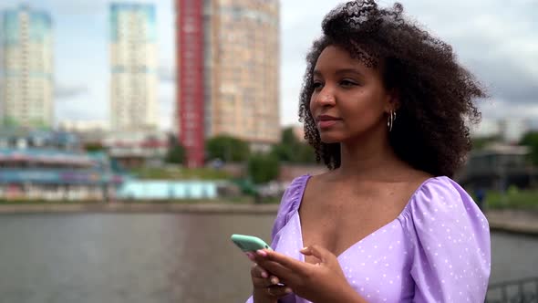 Young Black Woman Is Browsing Social Nets By Smartphone on Street of Big City