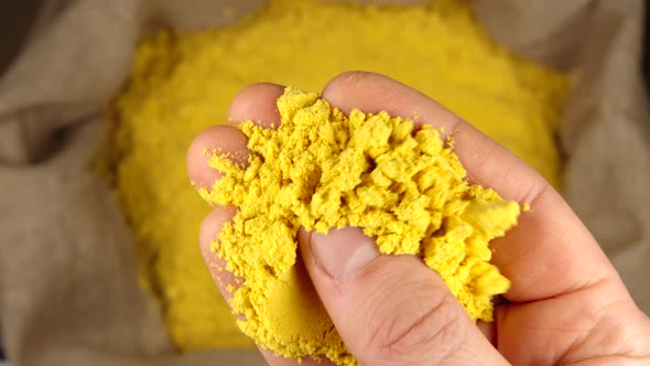 Human hand holds and presses a pinch of a turmeric (curcuma) powder over a sac