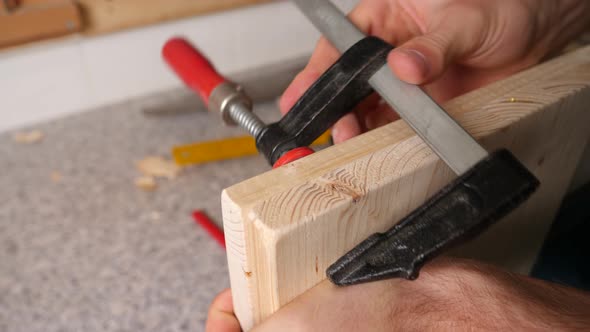 Caucasian hand of a diy worker screws two wooden plates with a screw clamp.