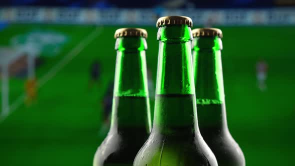 Three Green Glass Beer Bottles Spin Against the Backdrop of the Football Championship Broadcast