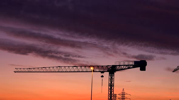 Black clouds glide gently at dusk over a construction crane alt