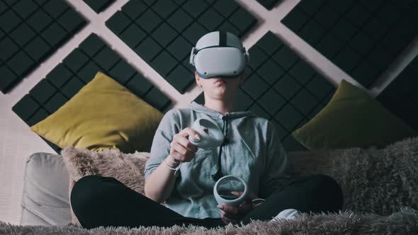 Young Woman in Virtual Reality Helmet Sitting on Sofa and Move Hands at Home