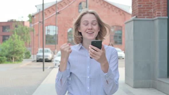 Woman Celebrating on Smartphone While Walking in Street