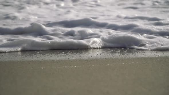 Super slow motion close up of wave and bubbles crashing on the beach on a sunny day