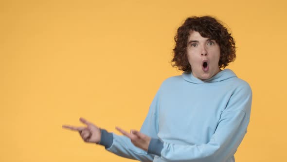 Slowmotion Impressed and Excited Cute Geeky Curly Young Guy Pointing Fingers Left Side Copy Space