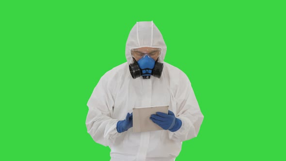 Epidemiologist in Hazmat Suit and Respirator Mask Using Digital Tablet While Walking on a Green