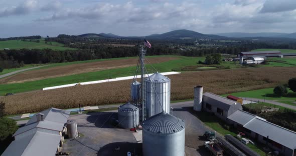 Aerial view pushing in towards American flag at top of grain silo with cornfields and mountains in t