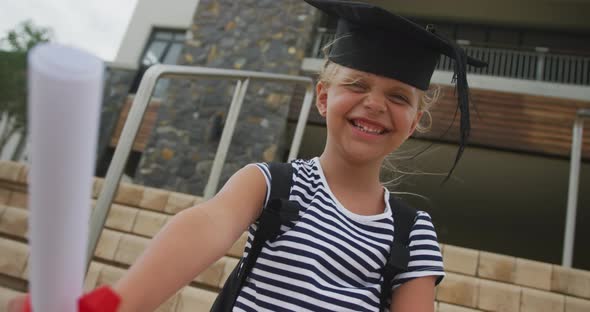 Video of happy caucasian girl wearing graduation hat and holding diploma