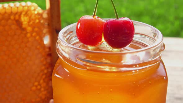 Sweet Cherry Is Dipped Into Honey in the Jar on the Background of the Honeycombs