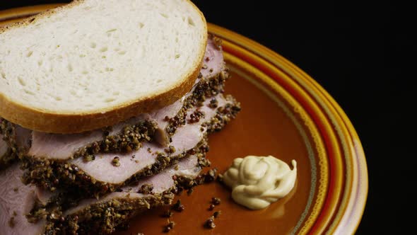 Rotating shot of delicious, premium pastrami sandwich next to a dollop of dijon mustard 