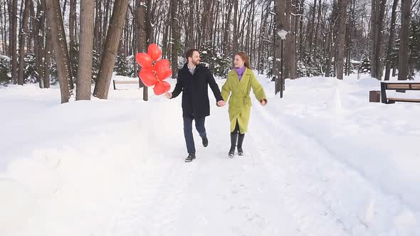 Romantic Couple in Love with Red Balloons Runs Through the Park on a Winter Day and Enjoys Time