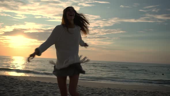 Happy Free Young Woman with Long Dark Hair in White Sweater Smiling Dancing Spinning with Stretched