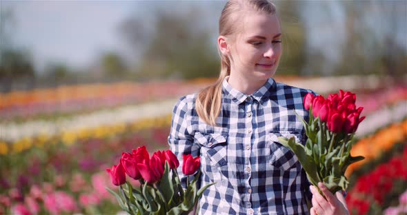 Woman Holding Tulips Bouquet in Hands While Walking on Tulips Field