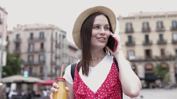 Young Adult Woman Talking on Phone While Drinking Orange Juice in the Street