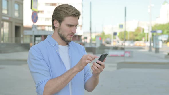 Upset Man Reacting to Loss on Smartphone Outdoor