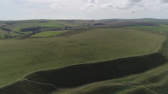 Aerial tracking around the edge of the iron age hill fort, Maiden Castle. Sheep are visible grazing