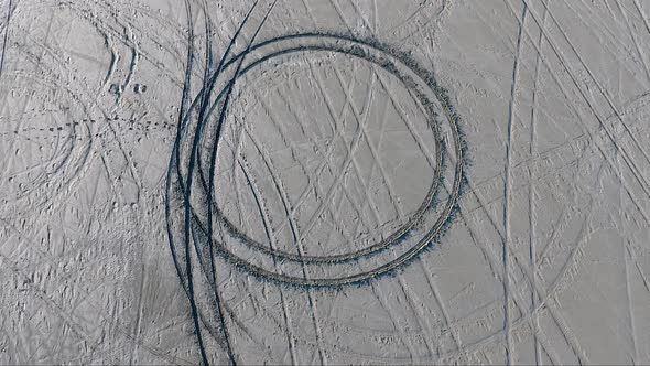 An aerial drone shot orbits a donut circle made by a car in the soft salt of the Bonneville Salt Fla