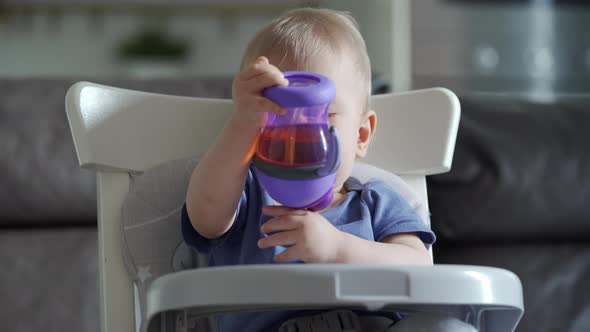 Cute Kid with Baby Straw Feeding Cup Sitting in Booster Seat One Year Old Toddler Watching Tv