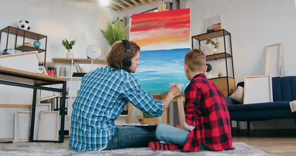 Boy Watching How His Father-Painter Drawing Picture on Canvas in Contemporary Sitting Room