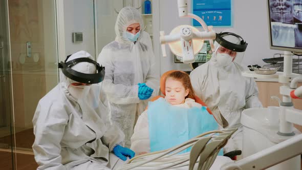 Little Patient in Ppe Suit Lying on Chair with Open Mouth During Dental Examination