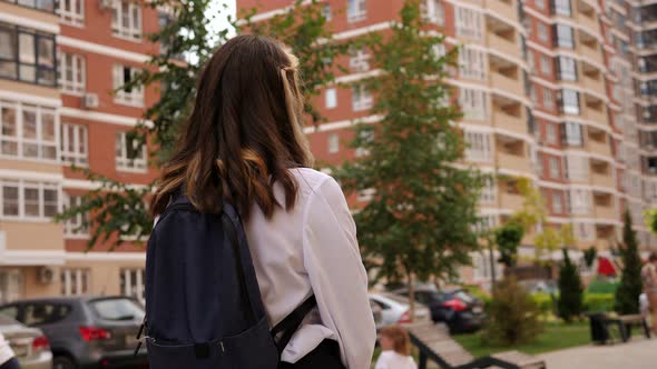 A View From the Back of a Teen Girl with a Backpack in the Courtyard of a House