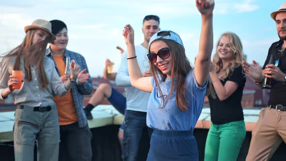 Young Woman Dancing in the Middle of Crowds with Raising Arms at Rooftop Party