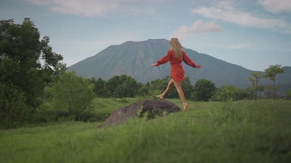 Carefree woman running towards boulder and taking in awe-inspiring view of Mount Agung, Savana Tiany