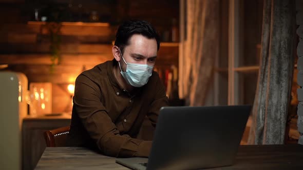 Young Man Wearing Respirator Is Typing on Laptop, Remote Working From Home.