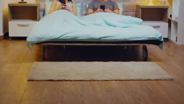 Bored Young Couple in Pajamas Using Smartphone