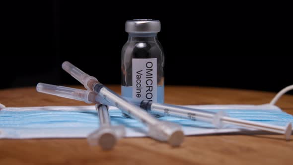 Close-up of a medical mask, syringes and vials of Omicron vaccine against a wooden background