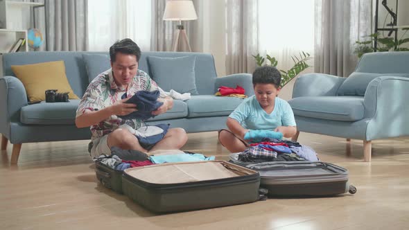 Asian Young Dad And Son Packing Clothes In Suitcase At Home, Preparing For Their Vacation