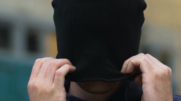 Aggressive Criminal Puts on Balaclava and Hood Hiding Face Before Attack, Danger