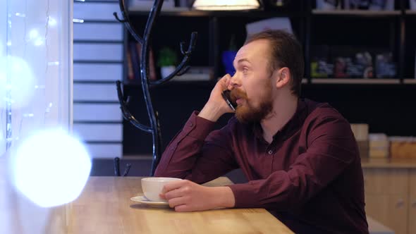 A man is talking on the phone with a friend or colleague and drink coffee.