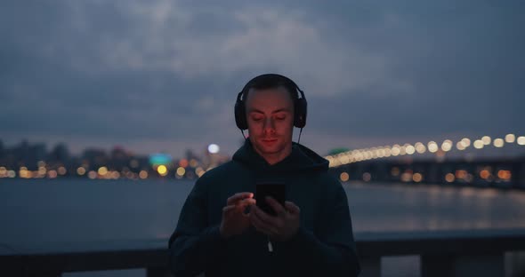 Man Using Phone in Headphones in Evening City