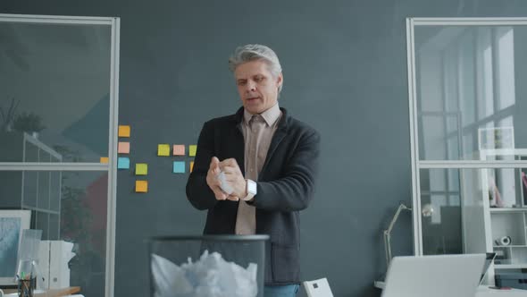 Portrait of Joyful Businessman Reading Contract Then Throwing Paper Ball in Trash Basket Having Fun