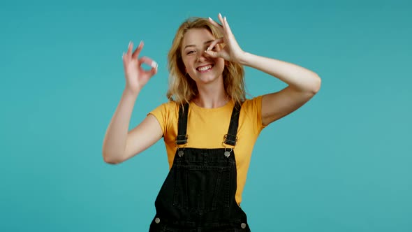 Cute Woman Showing Okay Sign Over Blue Background. Positive Young Girl Smiles To Camera. Winner