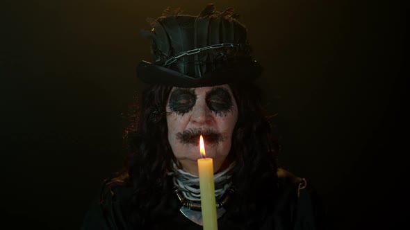 Sinister Elderly Woman with Horrible Scary Halloween Witch Vampire Makeup in Costume Holds a Candle