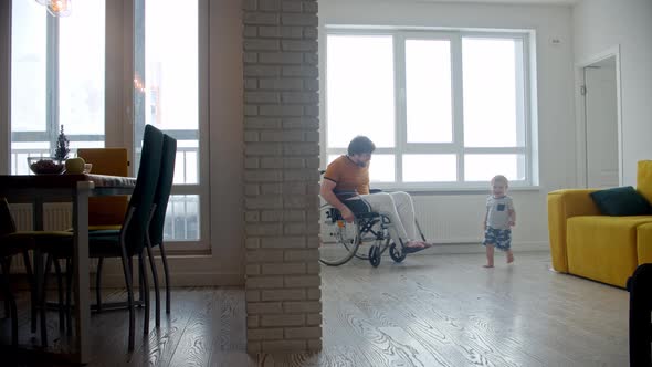 Man in a Wheelchair Follows His Little Running Baby Son Indoors