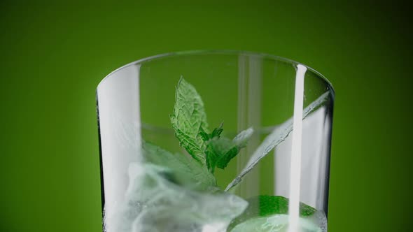 Leaf of Mint Drops to the Highbowl Glass with Cocktail and Ice Cubes on the Green Background 1080p