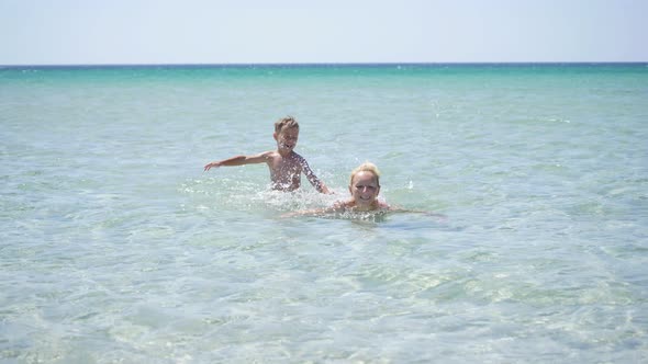 Happy Child Splashes Water on His Mother in the Sea