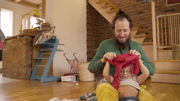 Father changing clothes of infant son at living room.