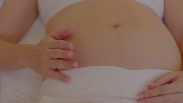 Happy Pregnant Woman sitting on bed holding and stroking her big belly at home